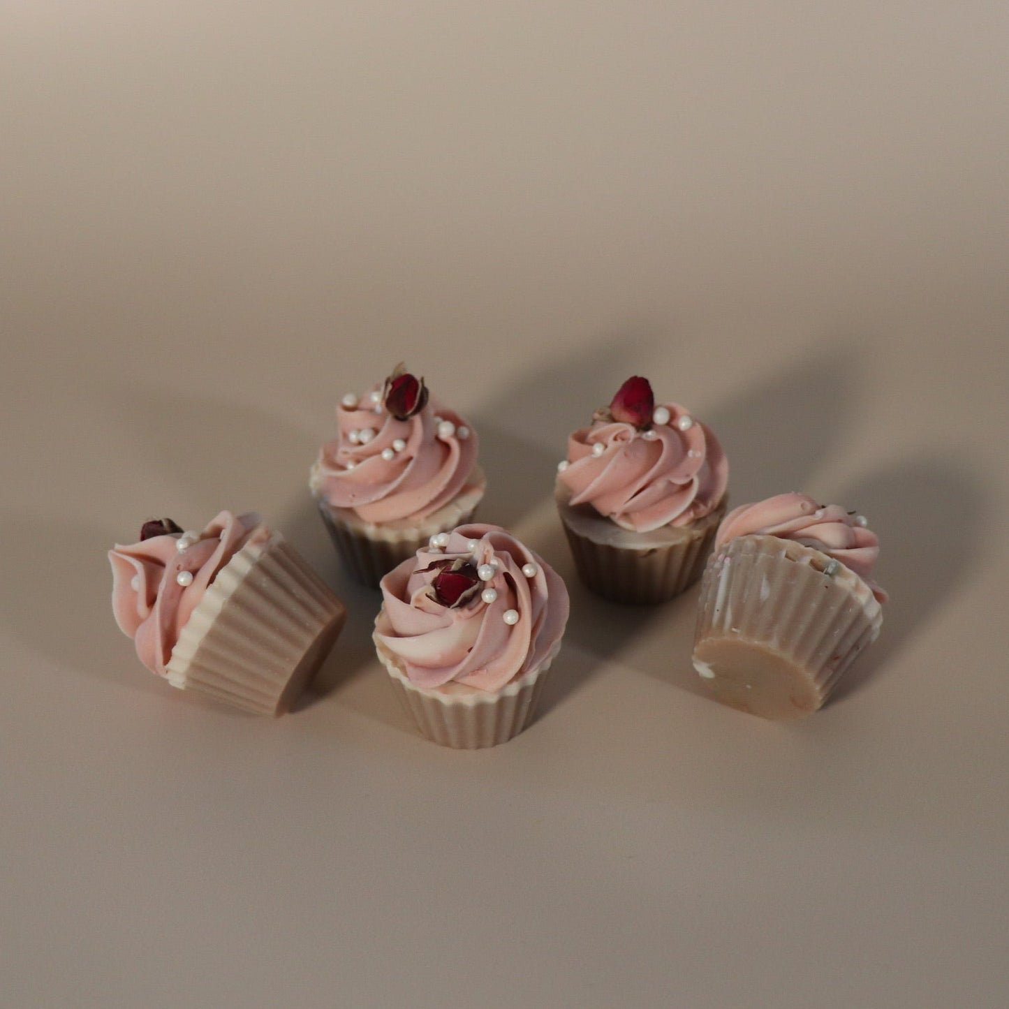 Five cupcake soaps with pink frosting and rose buds on a beige background