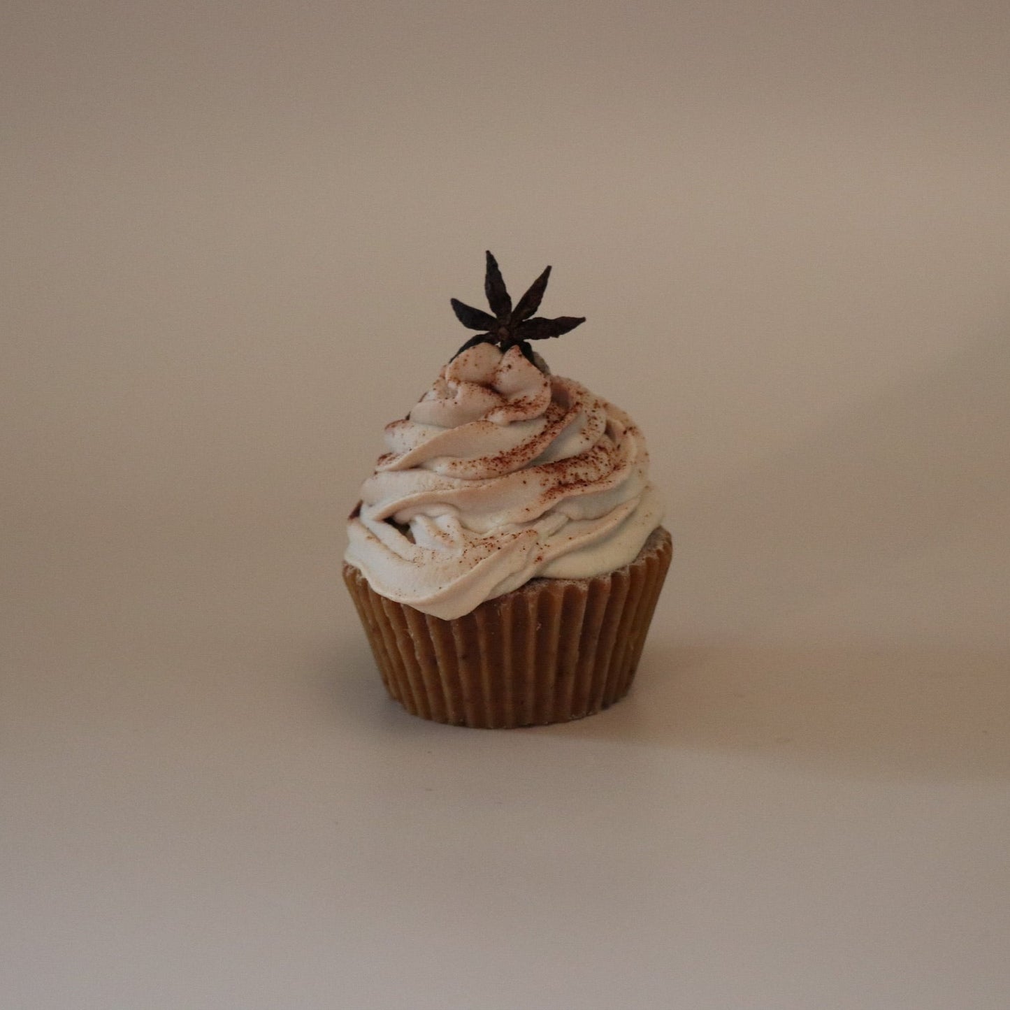 Cupcake with white frosting and a star-shaped decoration on a beige background