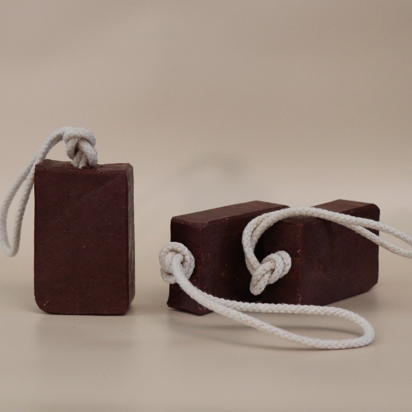 Two dark red soap bars with white ropes on a beige background