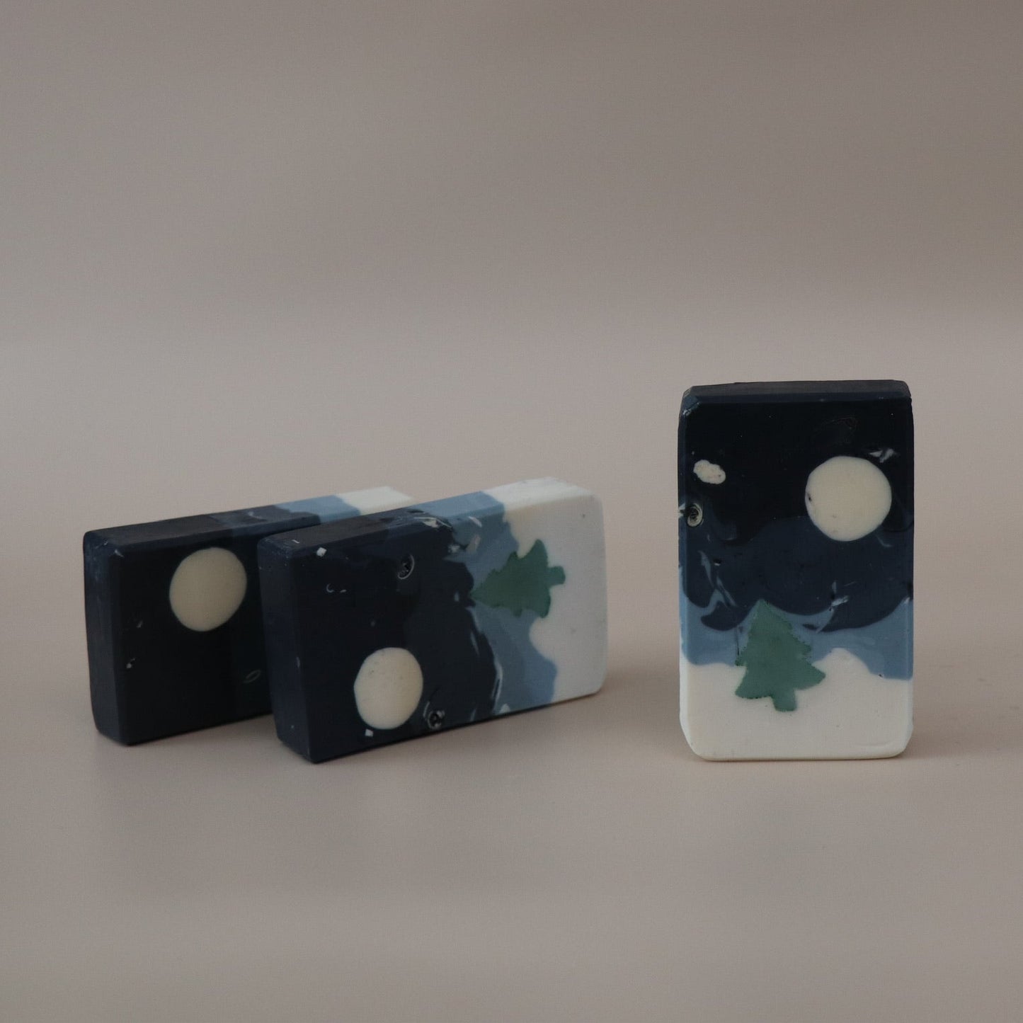 Three decorative stones with night sky and moon designs on a plain background