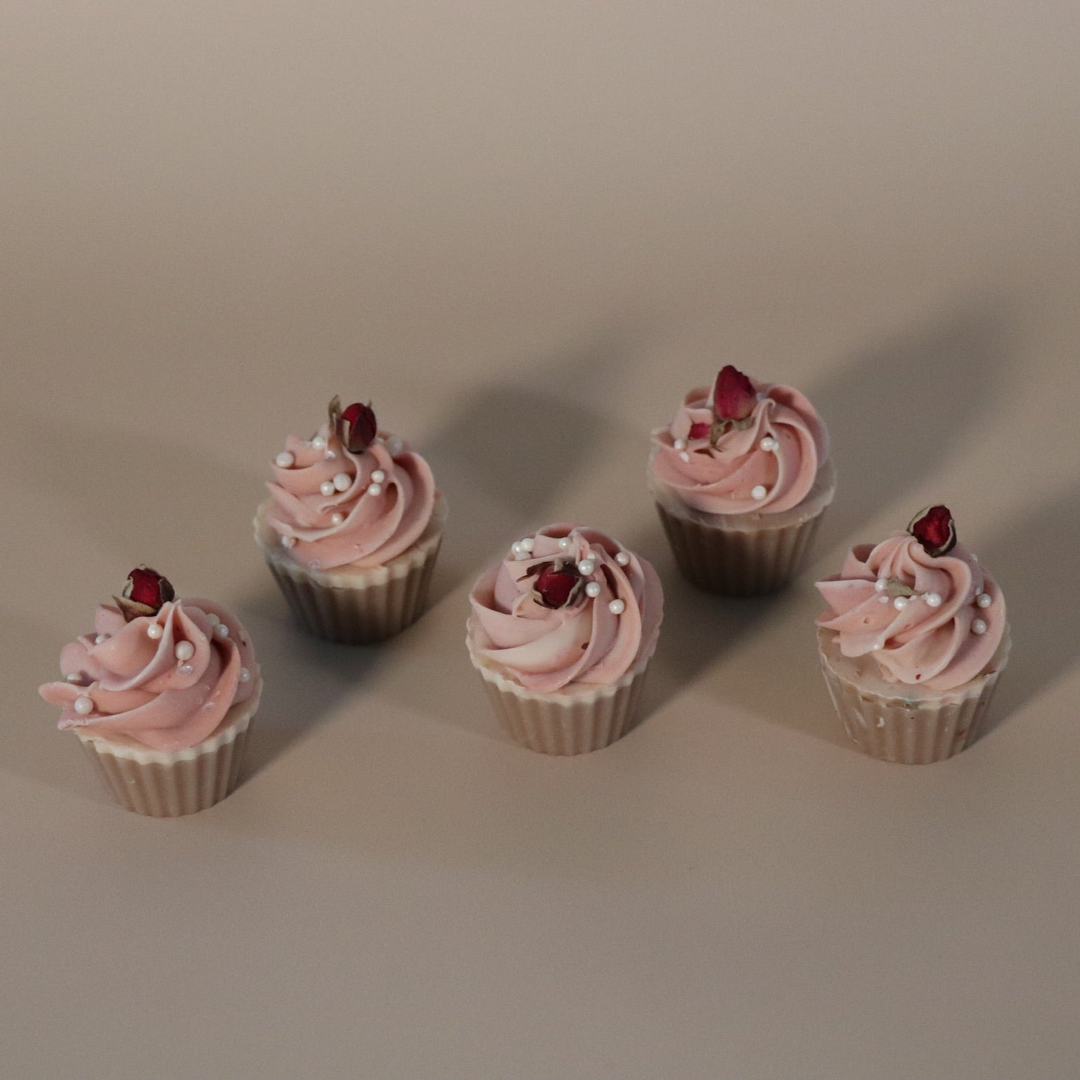 Five cupcake soaps with pink frosting and rose buds on a beige background