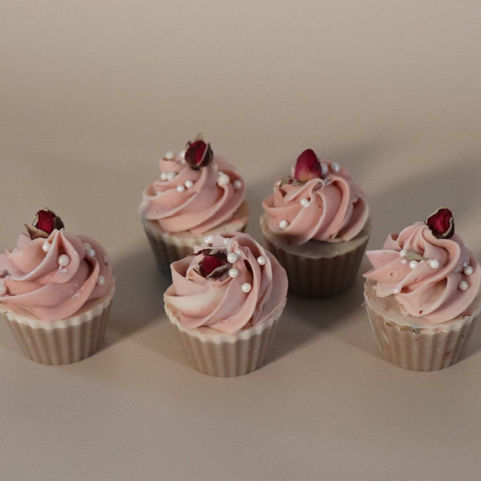Five cupcake soaps with pink frosting and rose buds on a beige background
