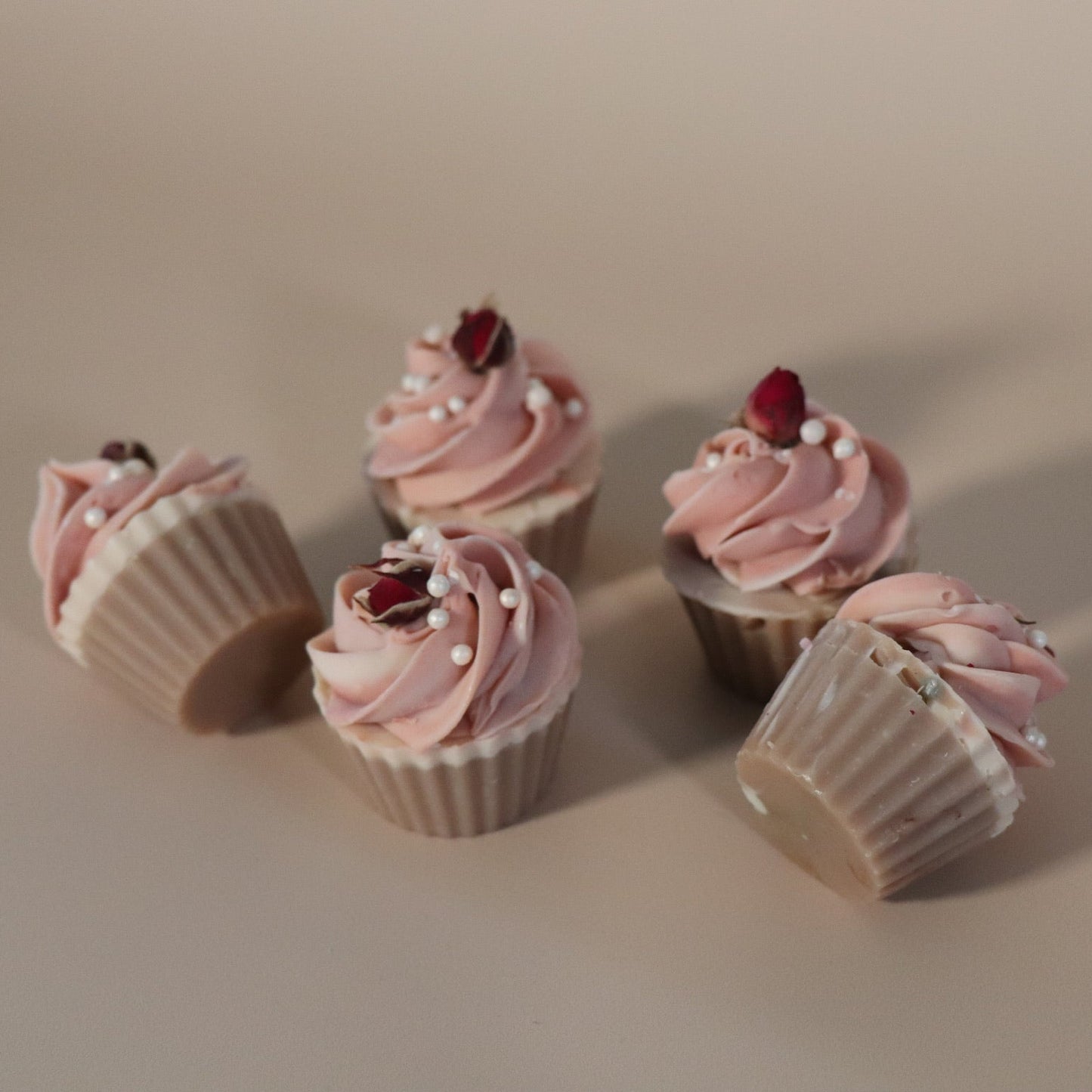 Five cupcake soaps with pink frosting and decorative elements on a beige background
