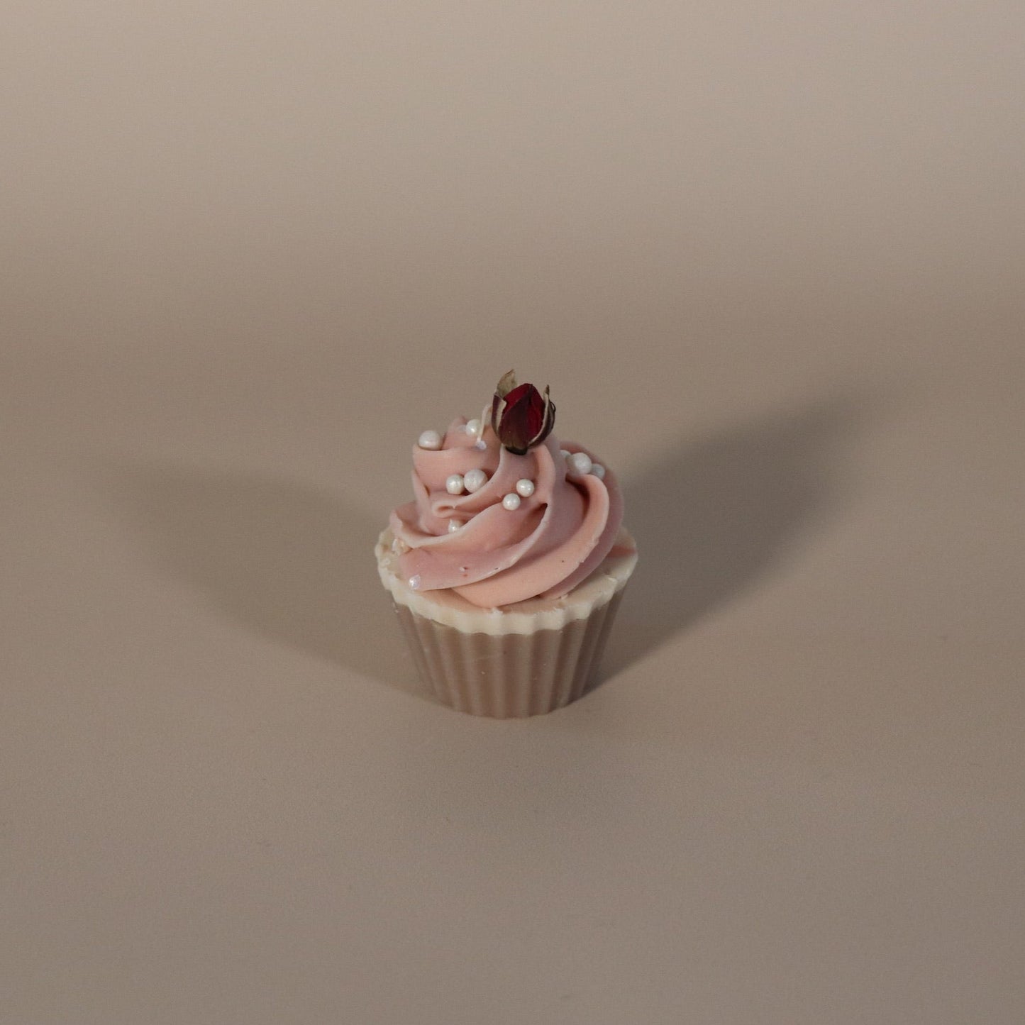 Cupcake soap with pink frosting and a rose bud on a beige background
