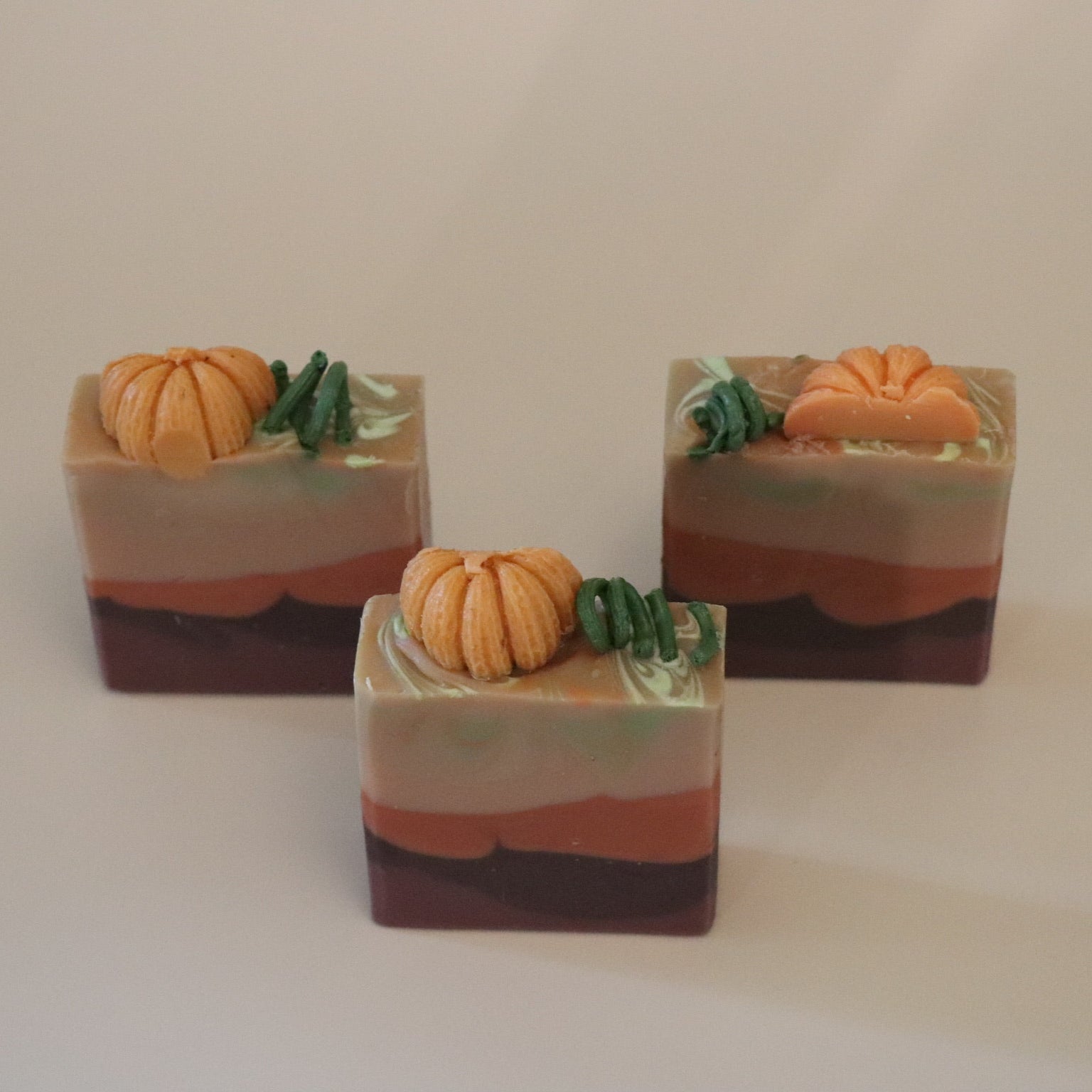 Three soap bars with pumpkin decorations on it and a beige background
