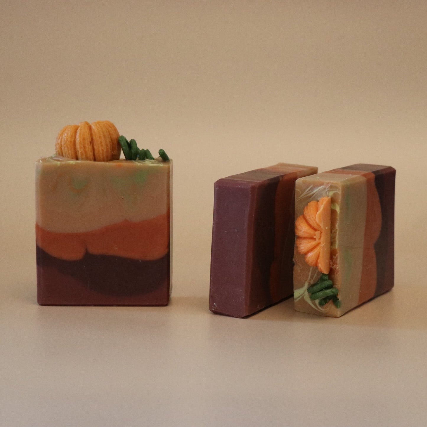 Three handmade soap bars with pumpkin decorations on it and a beige background