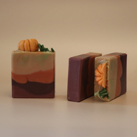 Three handmade soap bars with pumpkin decorations on it and a beige background
