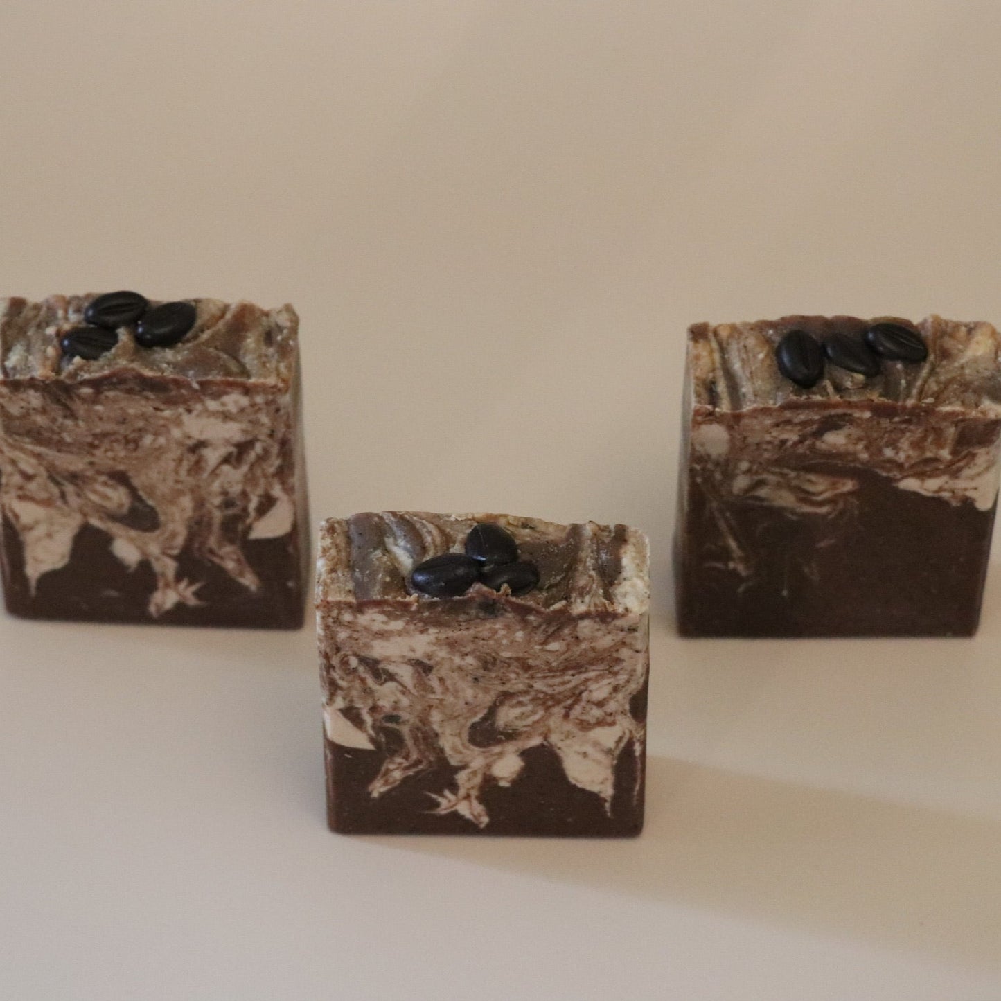 Three marbled brown and white soap bars with black specks on a beige background