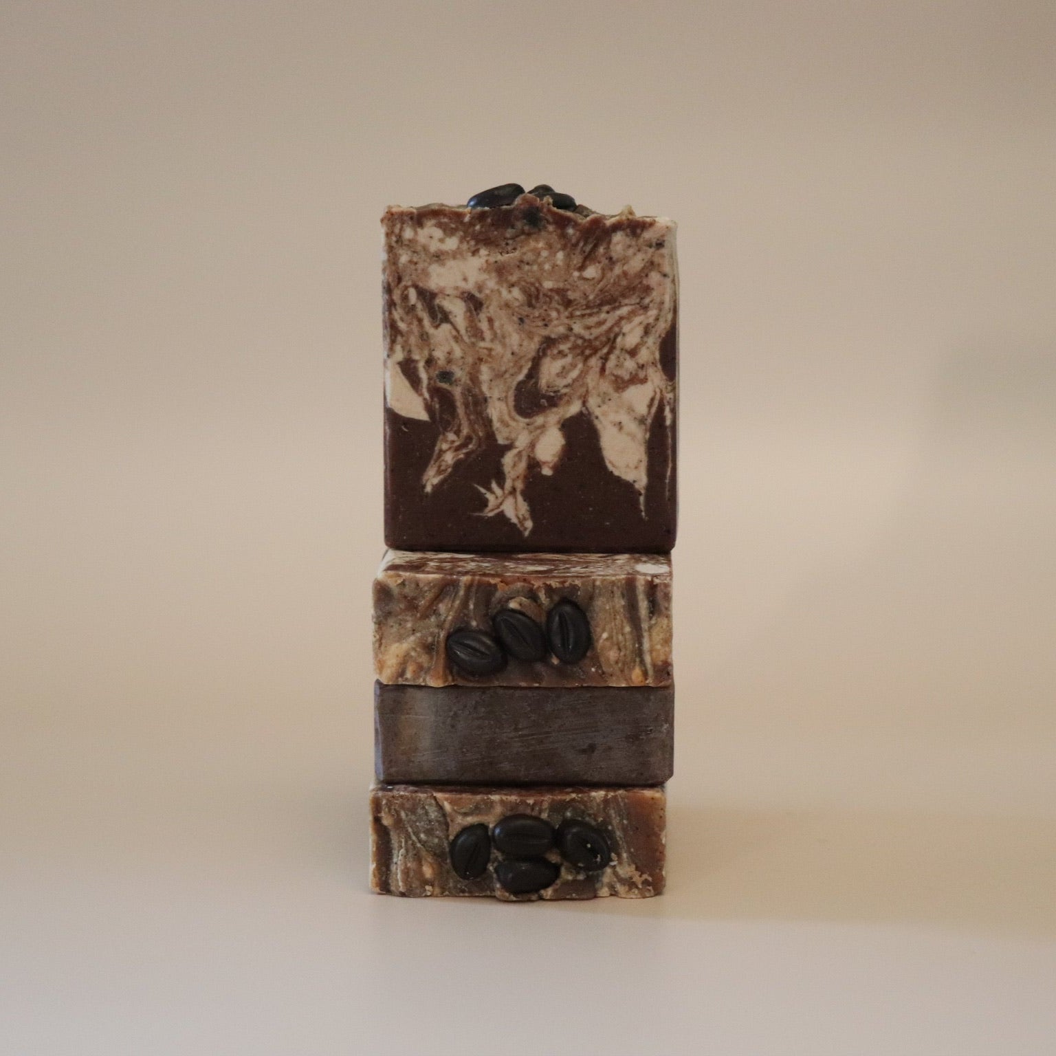 Three stacked soap bars with natural ingredients on a beige background