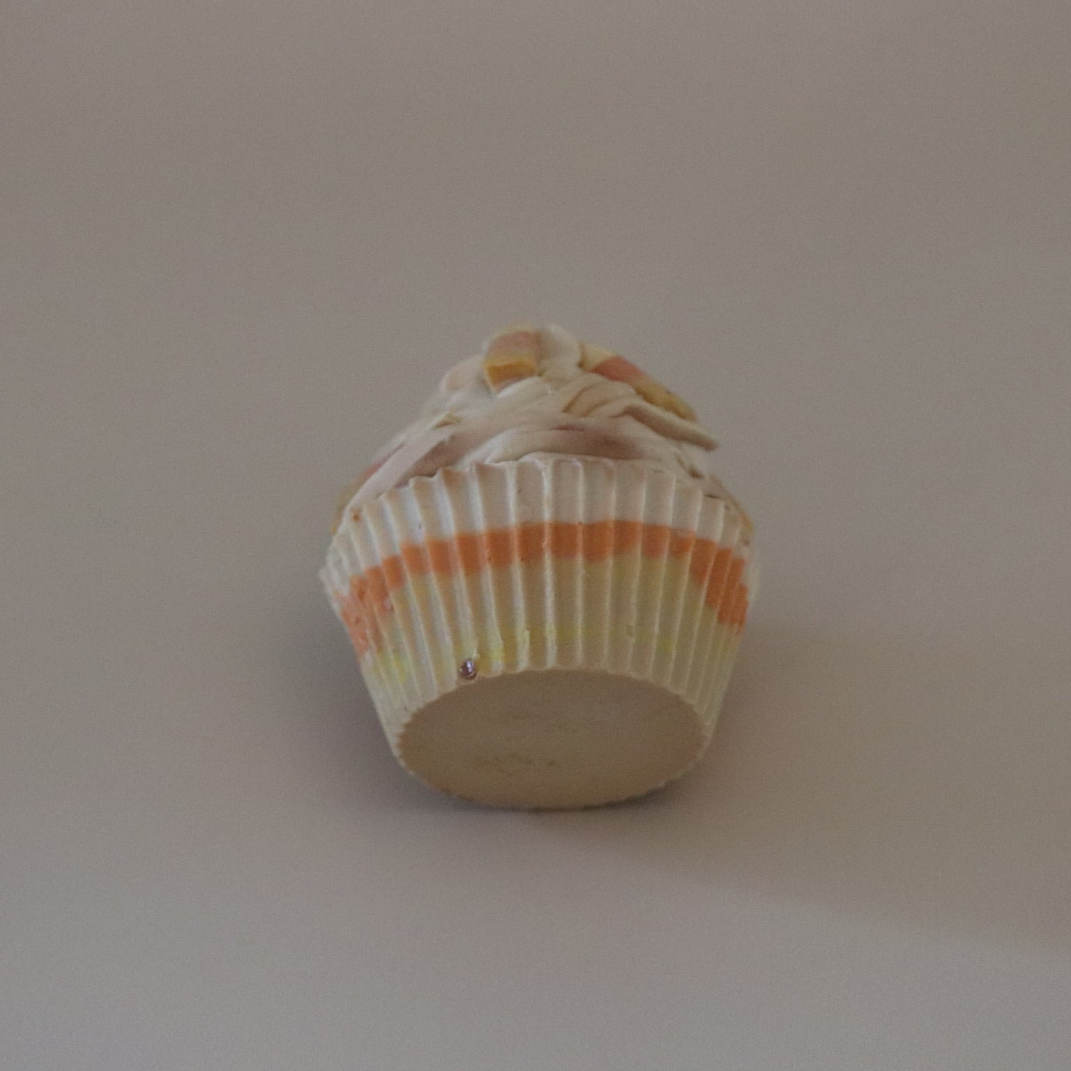 Cupcake soap bar with white frosting and a colorful paper liner on a plain background