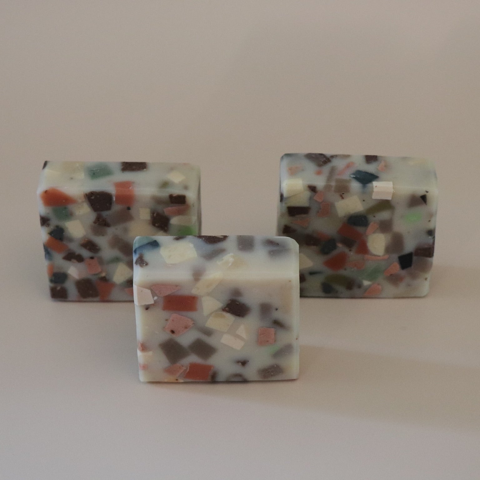 Three square-shaped, multicolored  terrazzo soap bars on a plain background