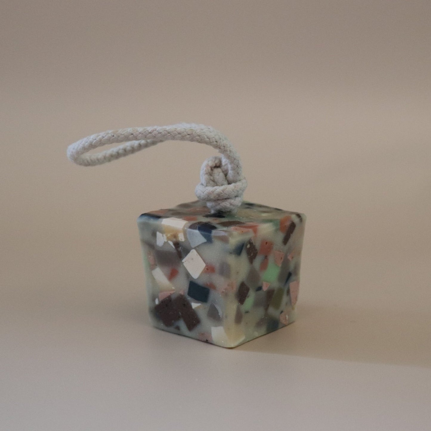 Colorful terrazzo cube-shaped soap on a rope against a beige background