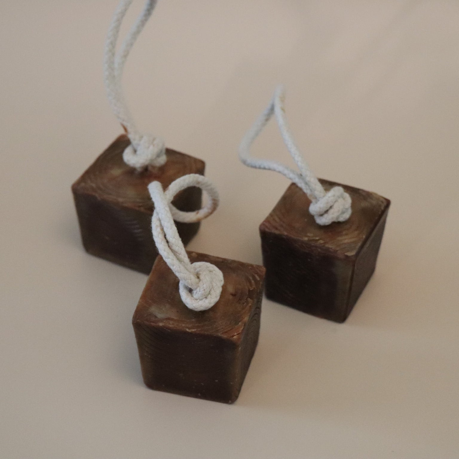Three wooden block soap bars with ropes tied to them on a beige background