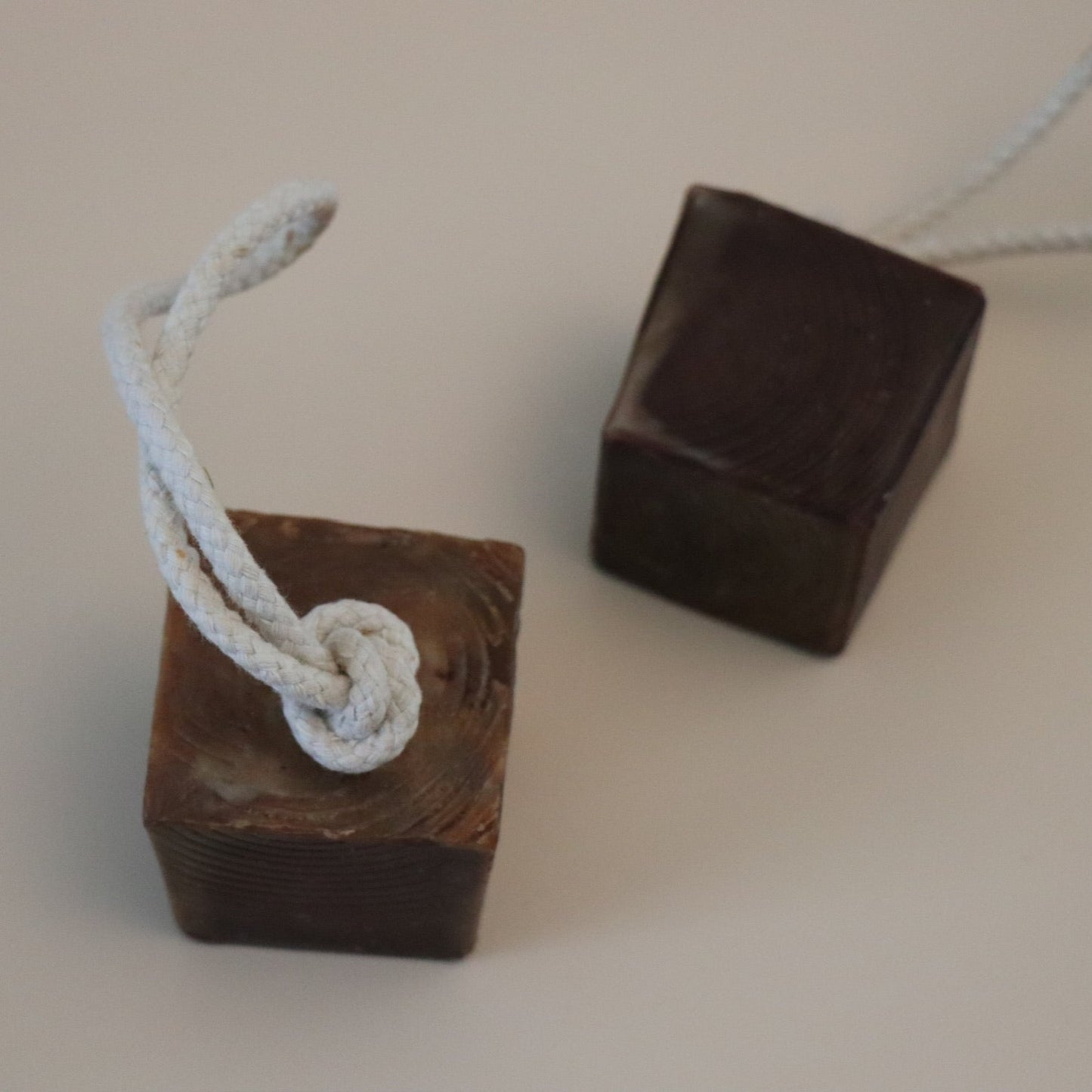 Two brown square cube soaps with white ropes tied to them on a beige background