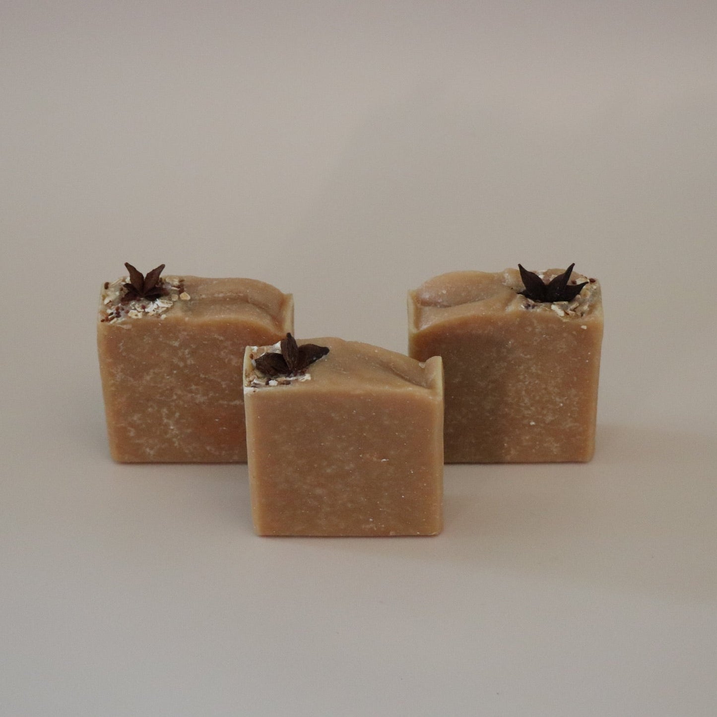 Three square-shaped brown soap bars with black specks on a beige background