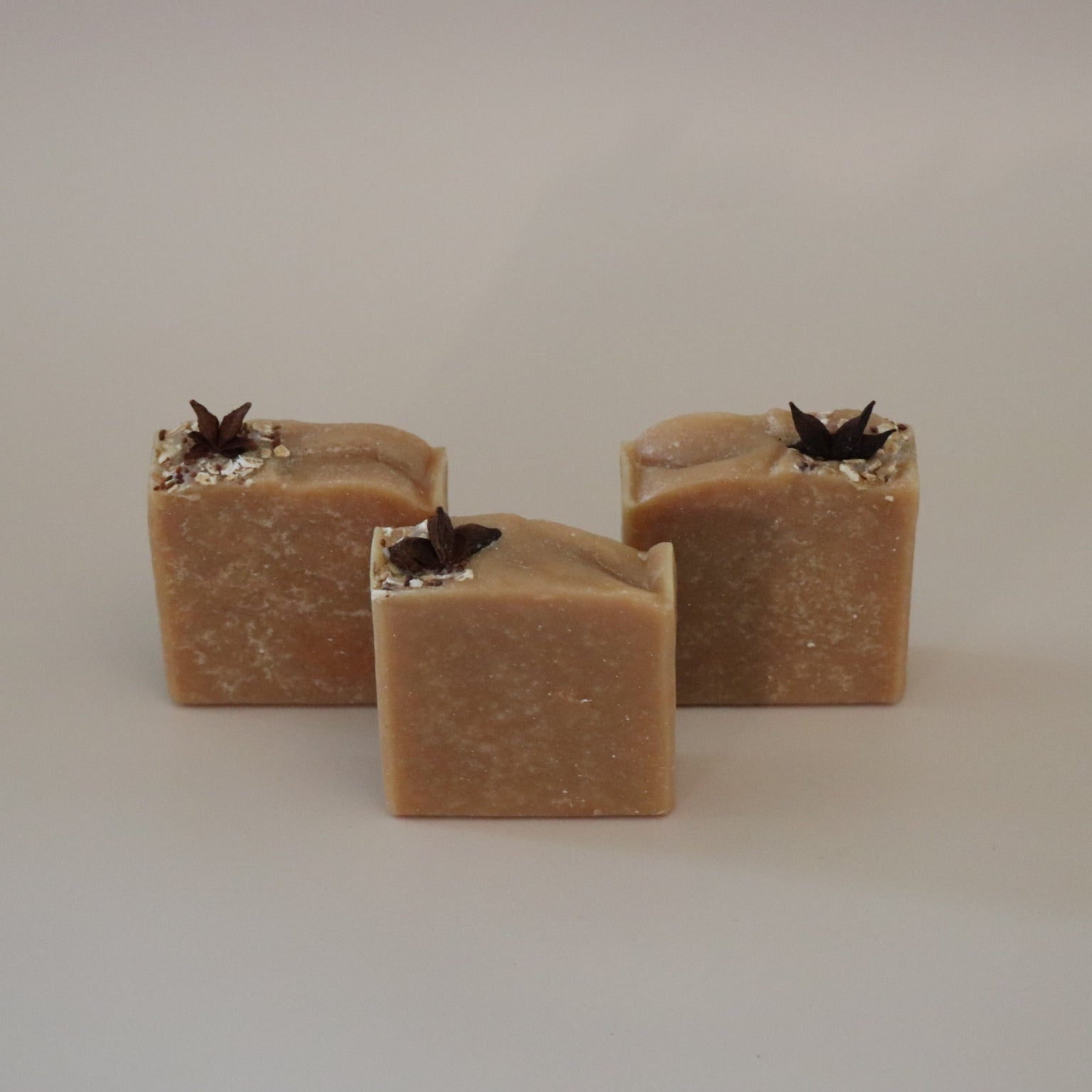 Three square-shaped brown soap bars with black specks on a beige background