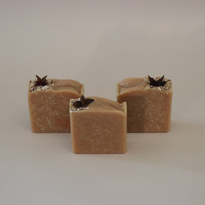 Three square-shaped brown soap bars with black specks on a beige background