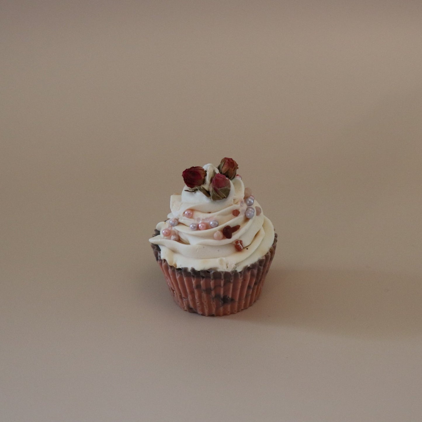 Cupcake with white frosting and red berries on a beige background