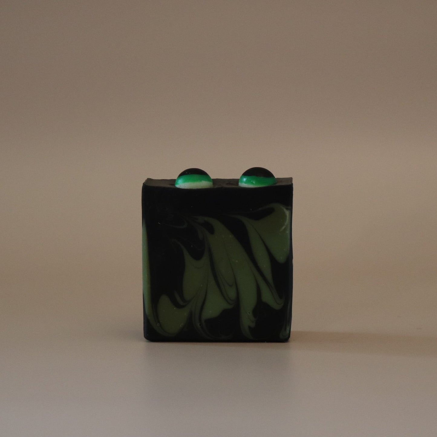 Black and green marbled soap bar with two green eyes on top on a beige background