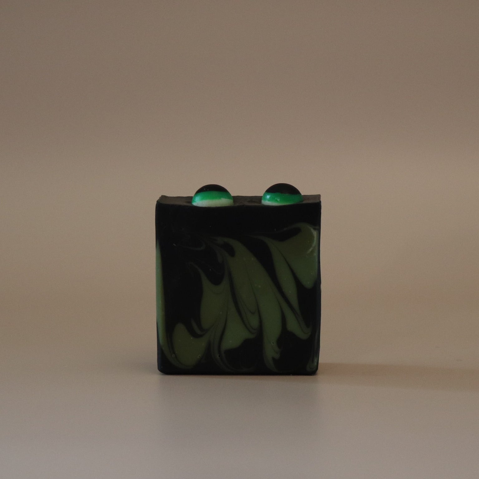 Black and green marbled soap bar with two green eyes on top on a beige background