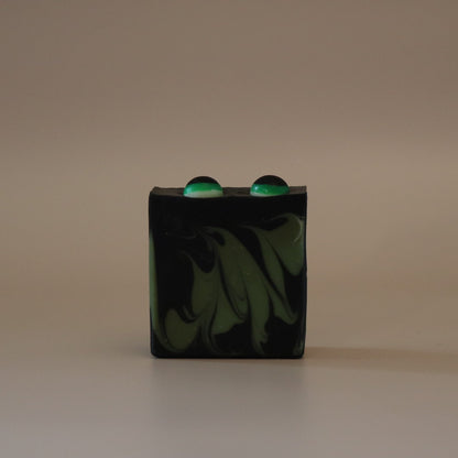 Black and green marbled soap bar with two green eyes on top on a beige background