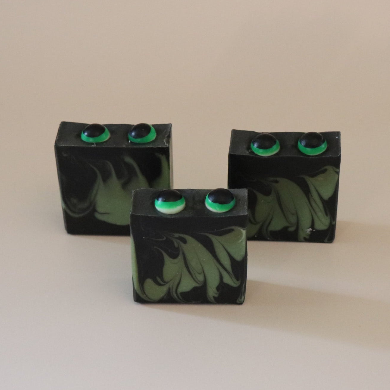 Three black and green soap bars on a beige background