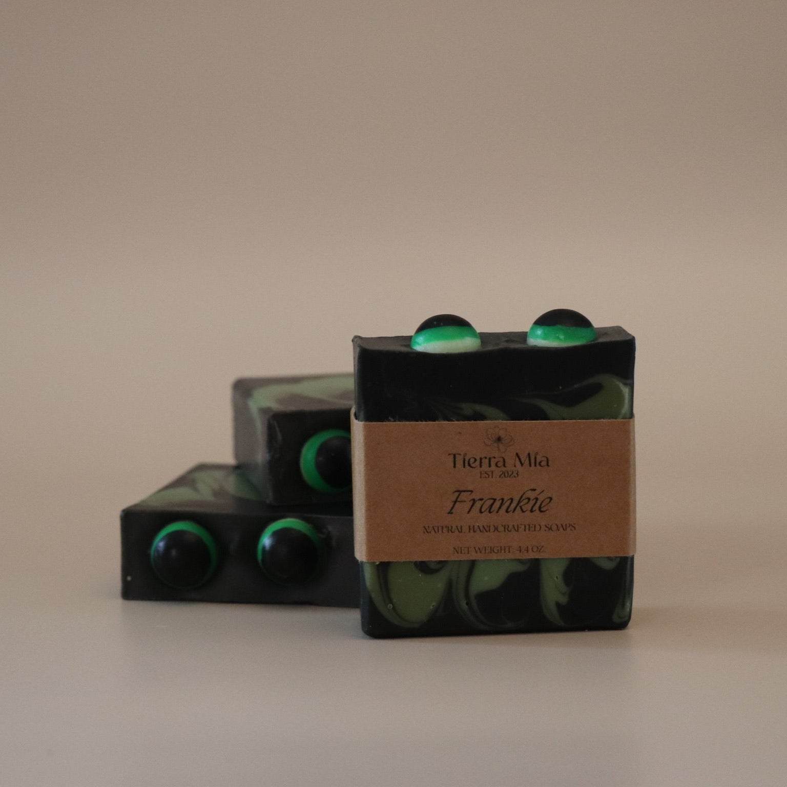Three black & green soap bars with a label on a beige background