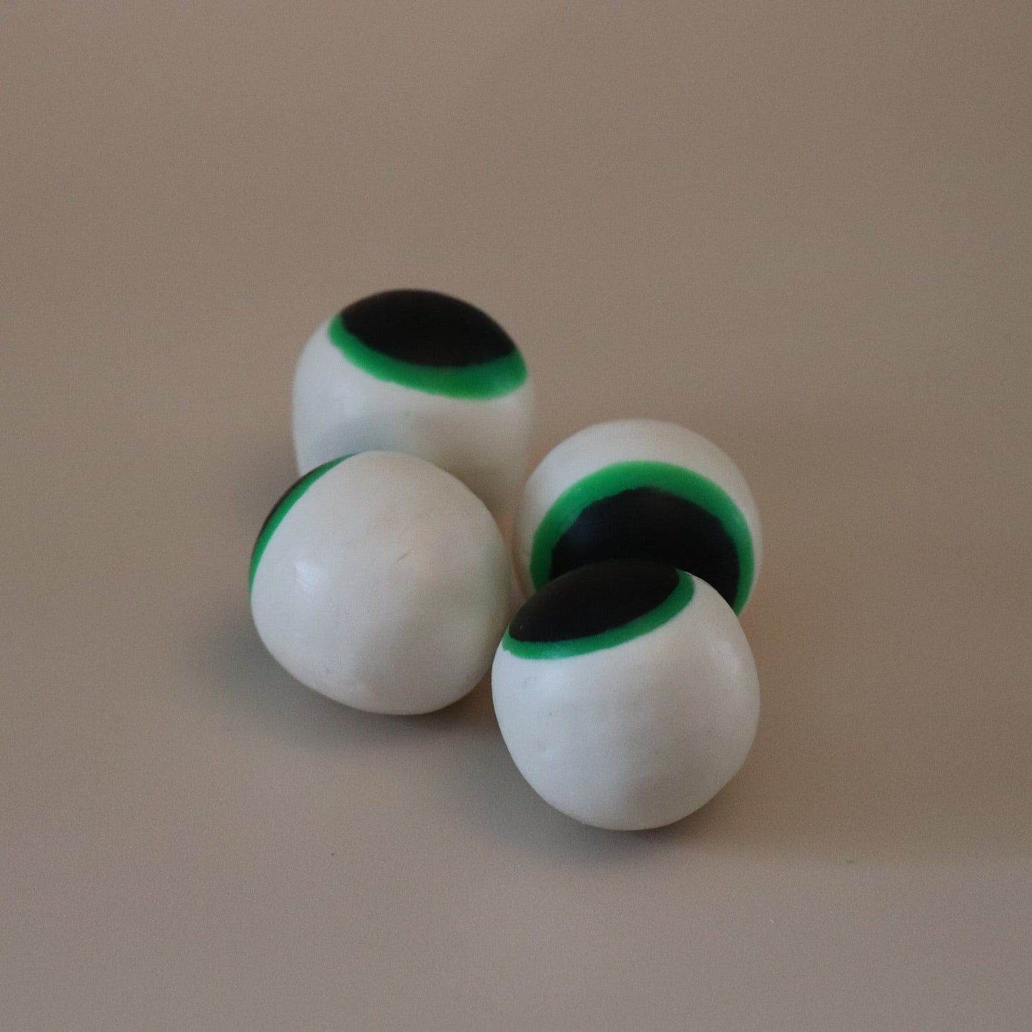 Four white eyeball soaps with green and black accents on a beige background