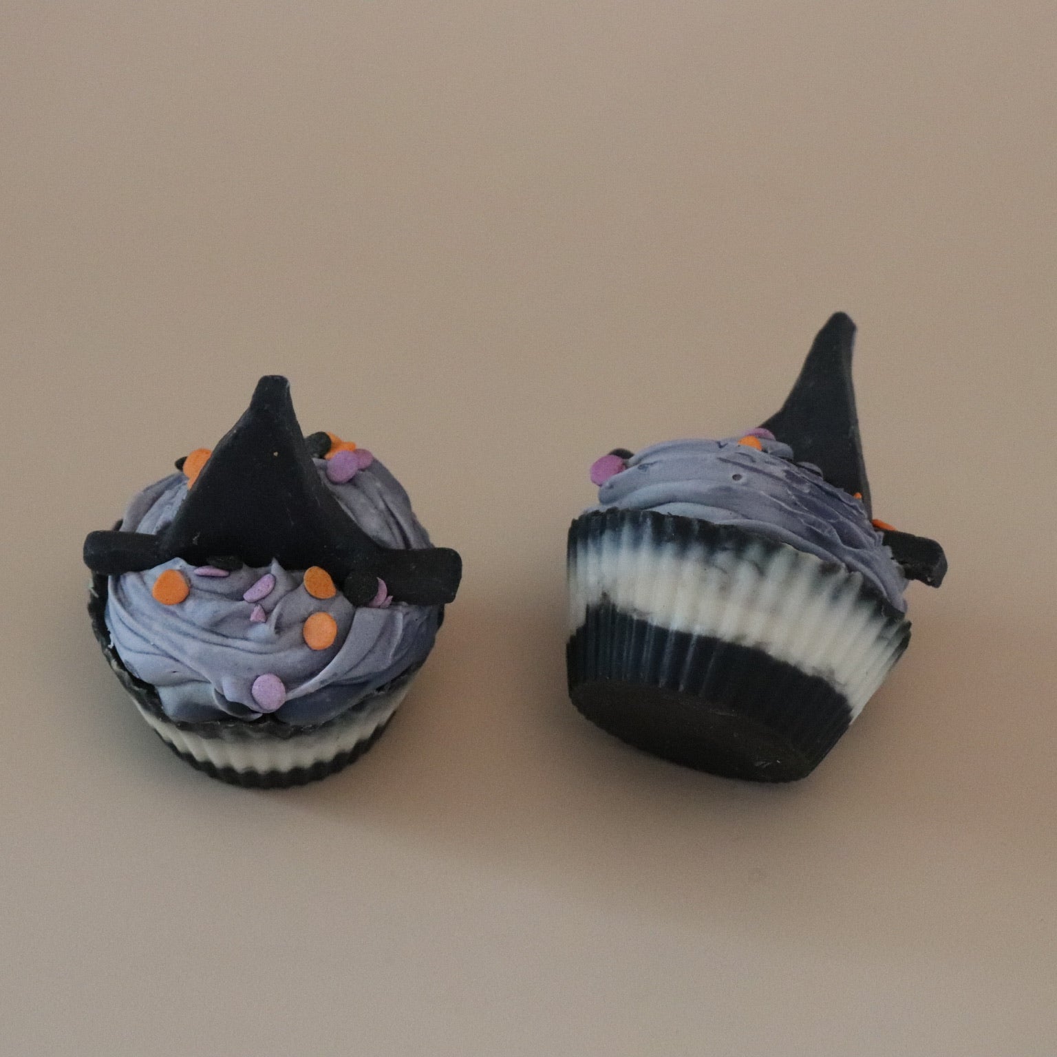 Two cupcake soaps decorated with witch hats on a beige background