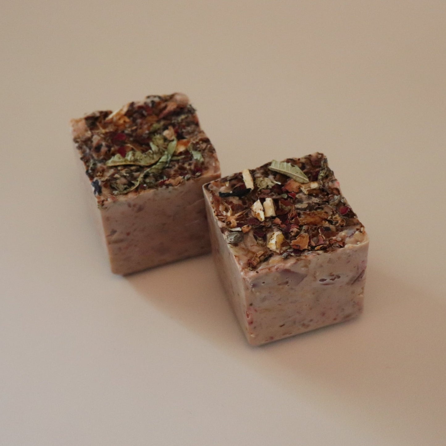 Two cube-shaped soap bars with visible potpourri on top on a beige background