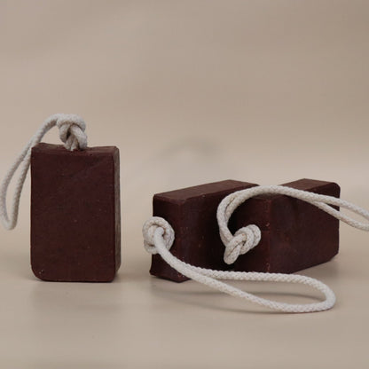 Two dark red soap bars with white ropes on a beige background