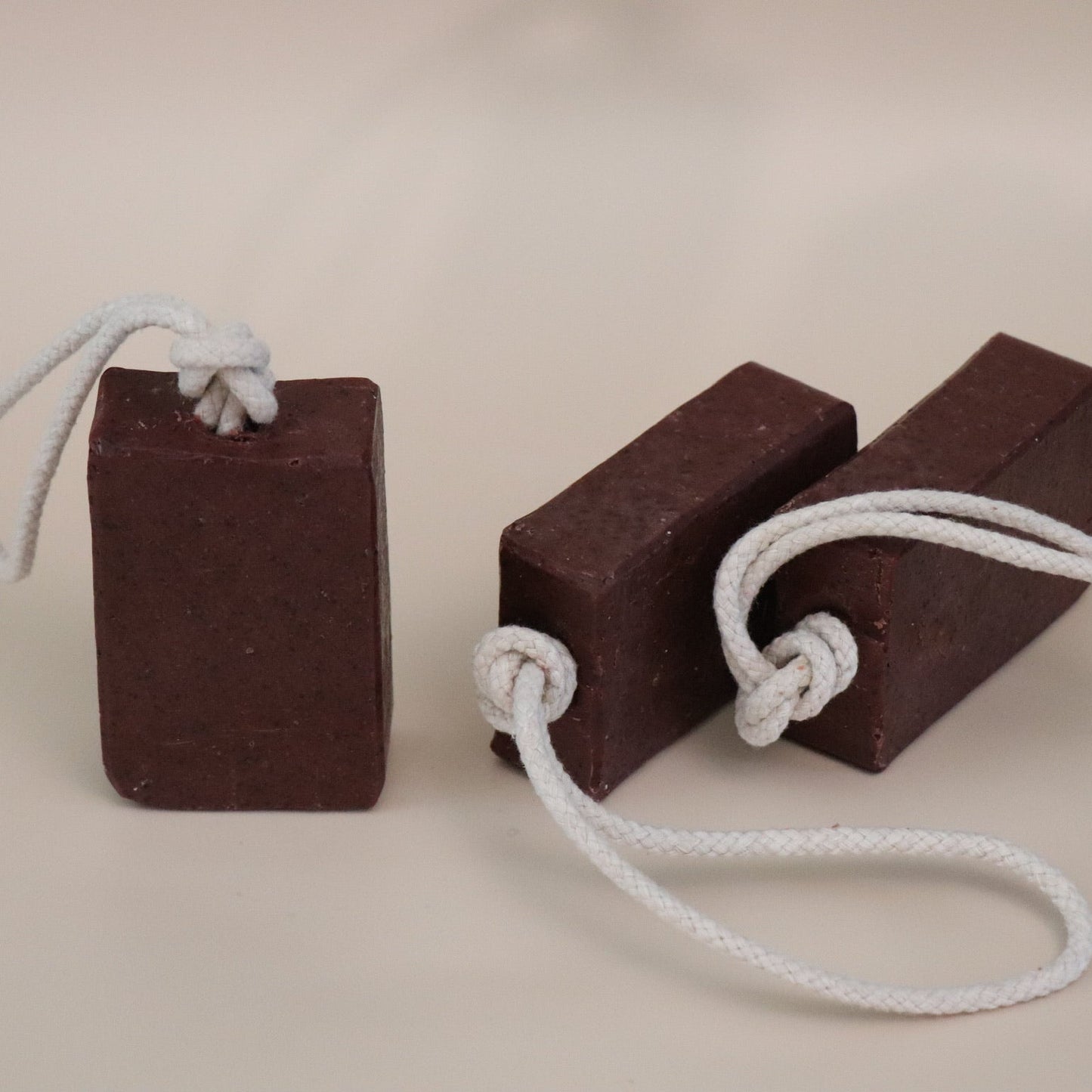 Two dark red soap bars with white ropes on a beige background