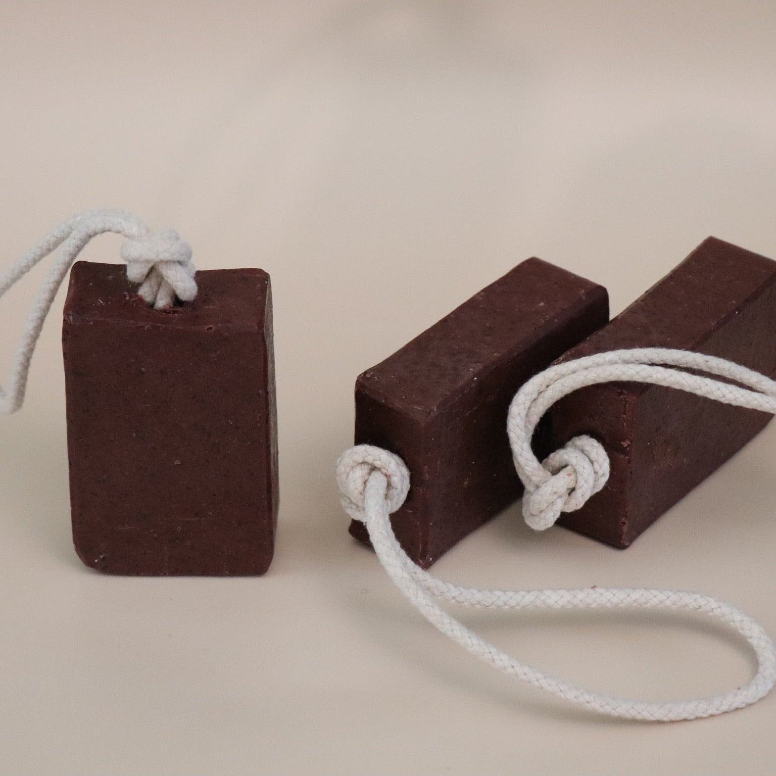 Two dark red soap bars with white ropes on a beige background