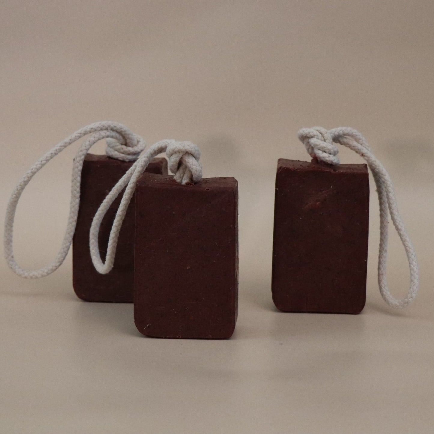 Three dark red soap bars with ropes on a beige background