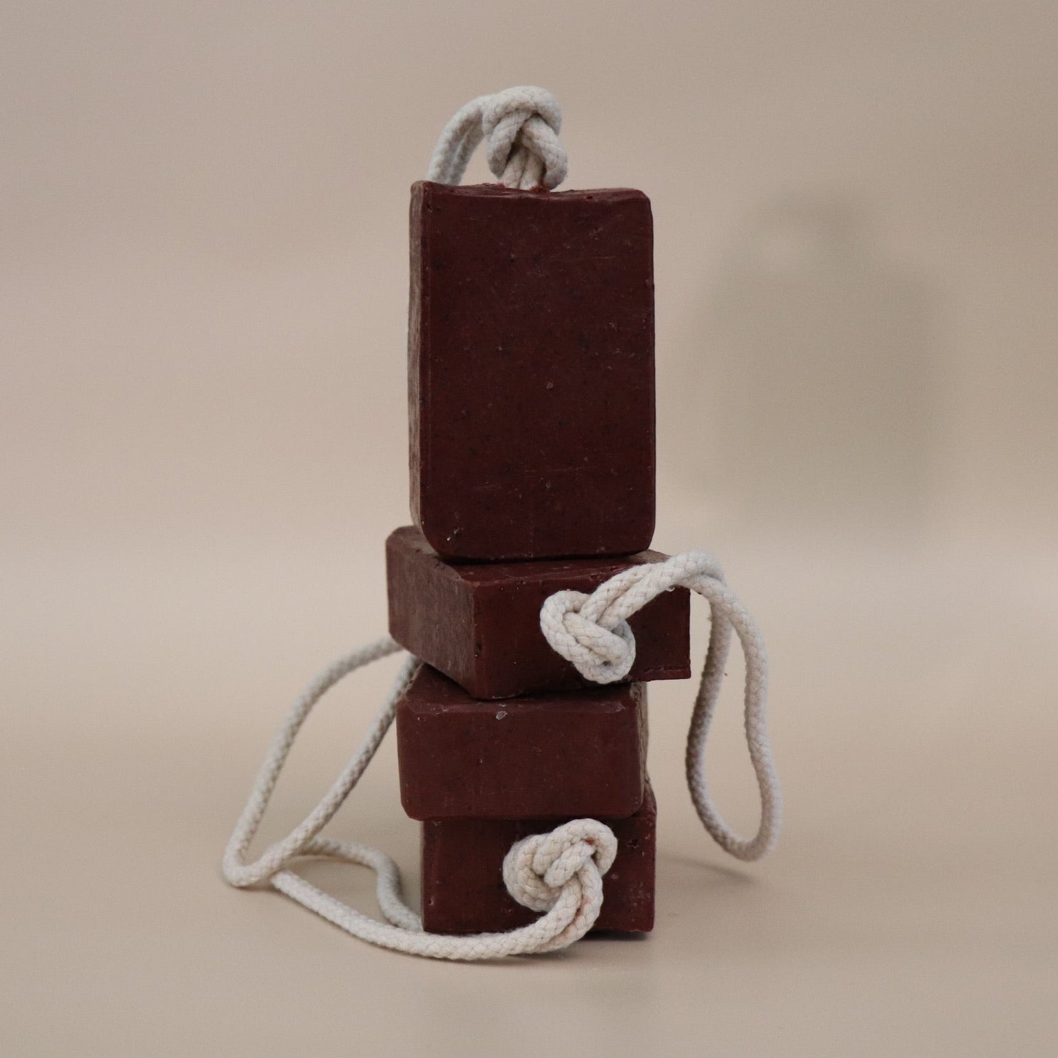 Three stacked dark red soap bars with white ropes on a beige background
