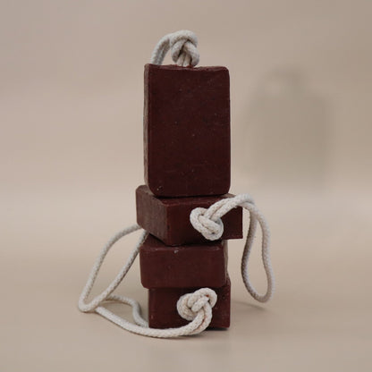 Three stacked dark red soap bars with white ropes on a beige background
