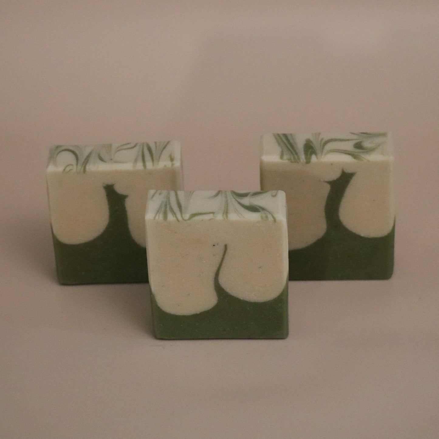 Three green and white soap bars with leaf pattern on a beige background