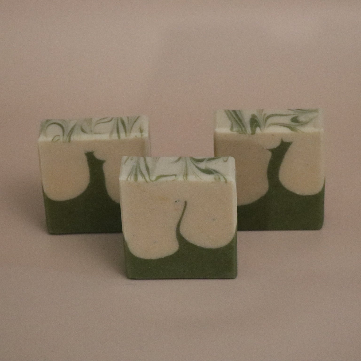 Three green and white soap bars with leaf pattern on a beige background