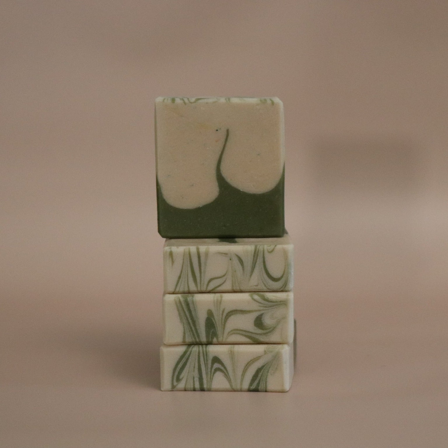 Stack of green soap bars with leaf patterns on a beige background