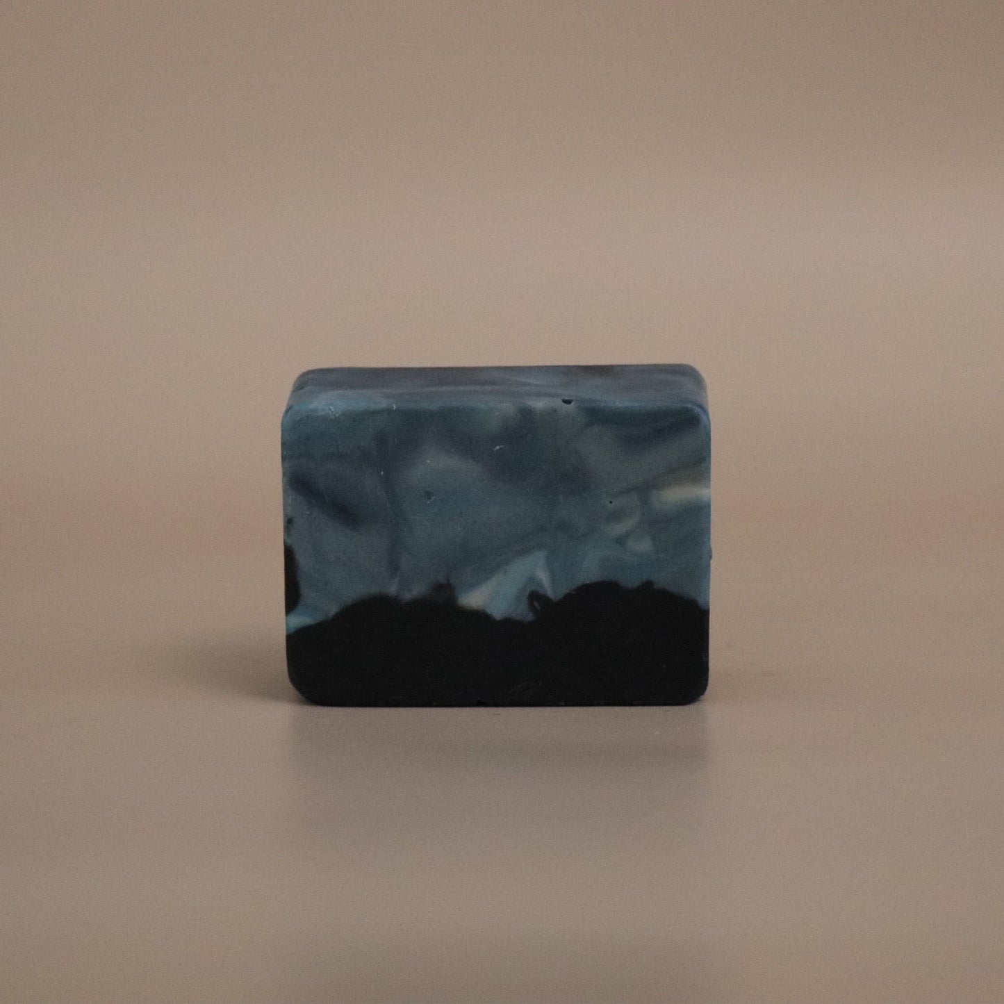 Bar of soap with black and blue marbled pattern on a beige background