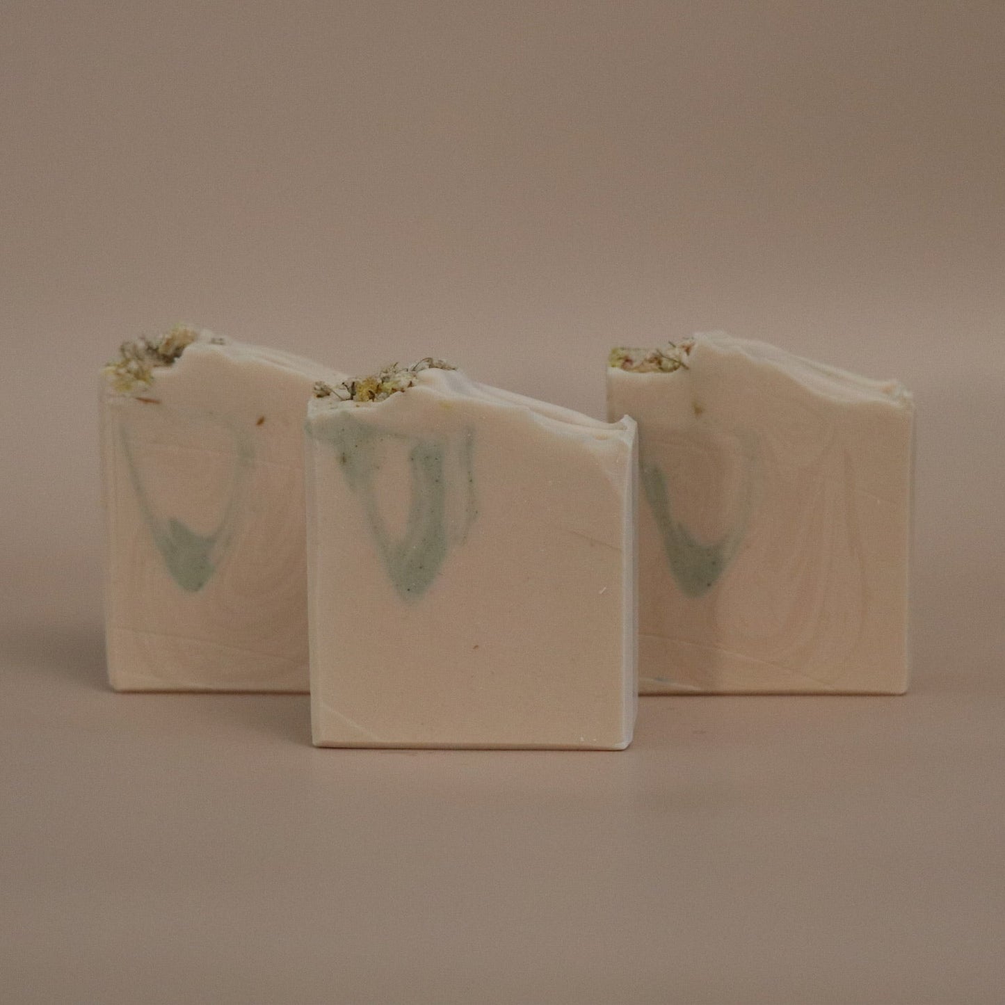 Three bars of soap with green swirls on a beige background