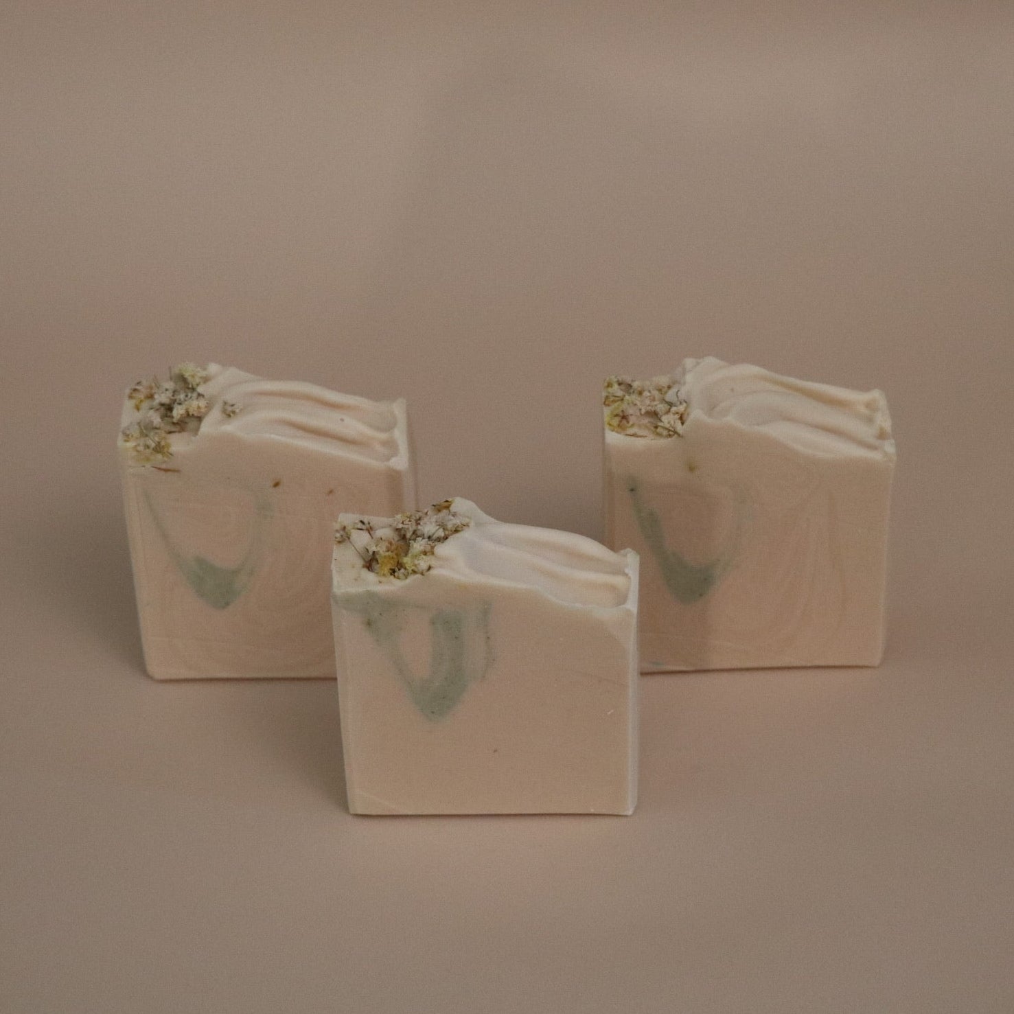 Three white soap bars with green and gold designs on a beige background