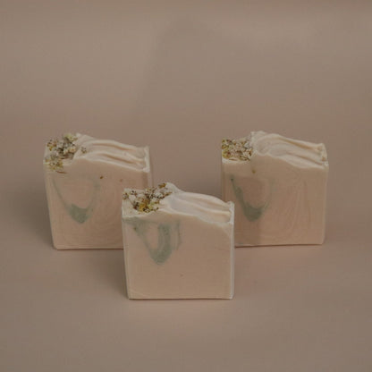 Three white soap bars with green and gold designs on a beige background