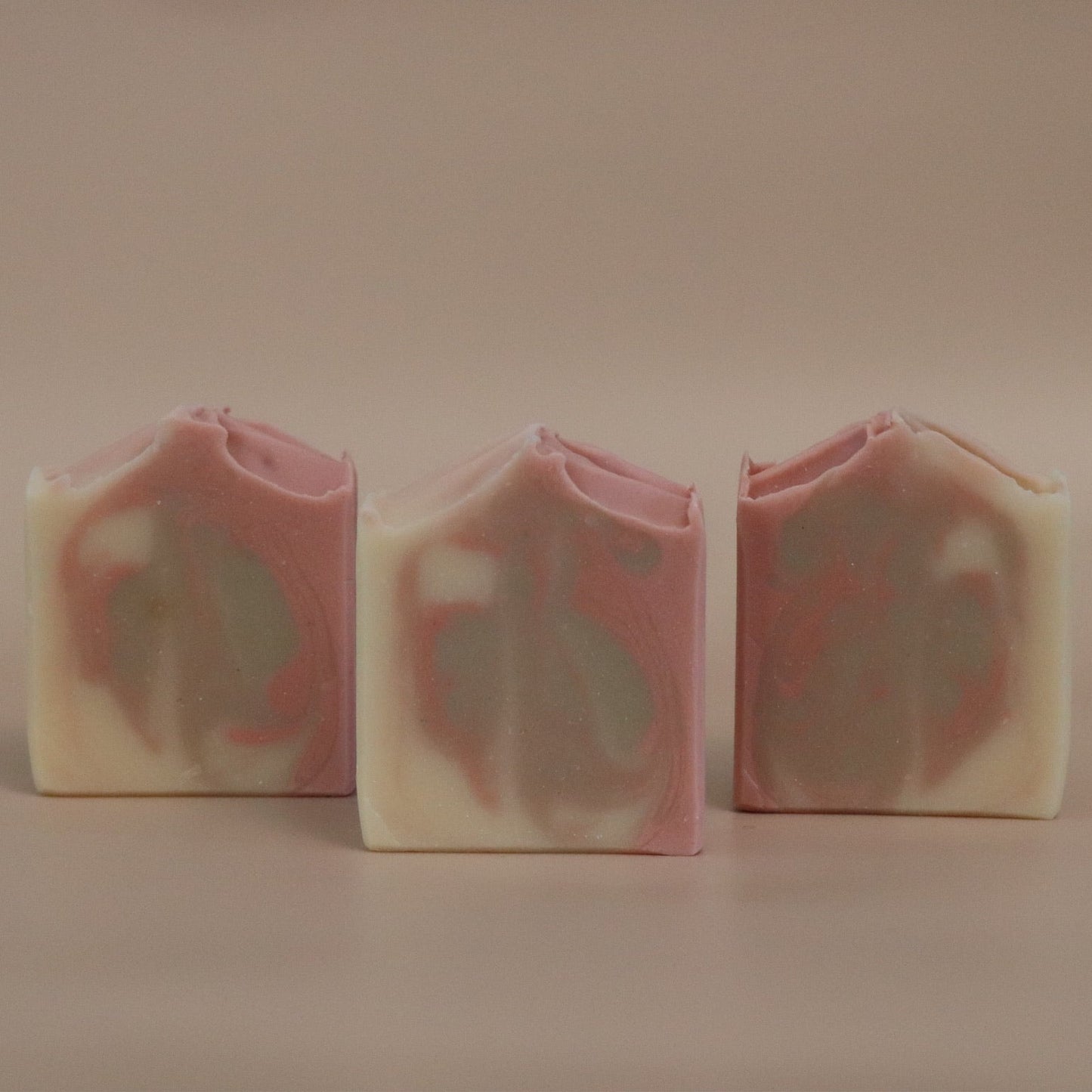 Three bars of soap with a pink, brown, and white marbled pattern on a beige background