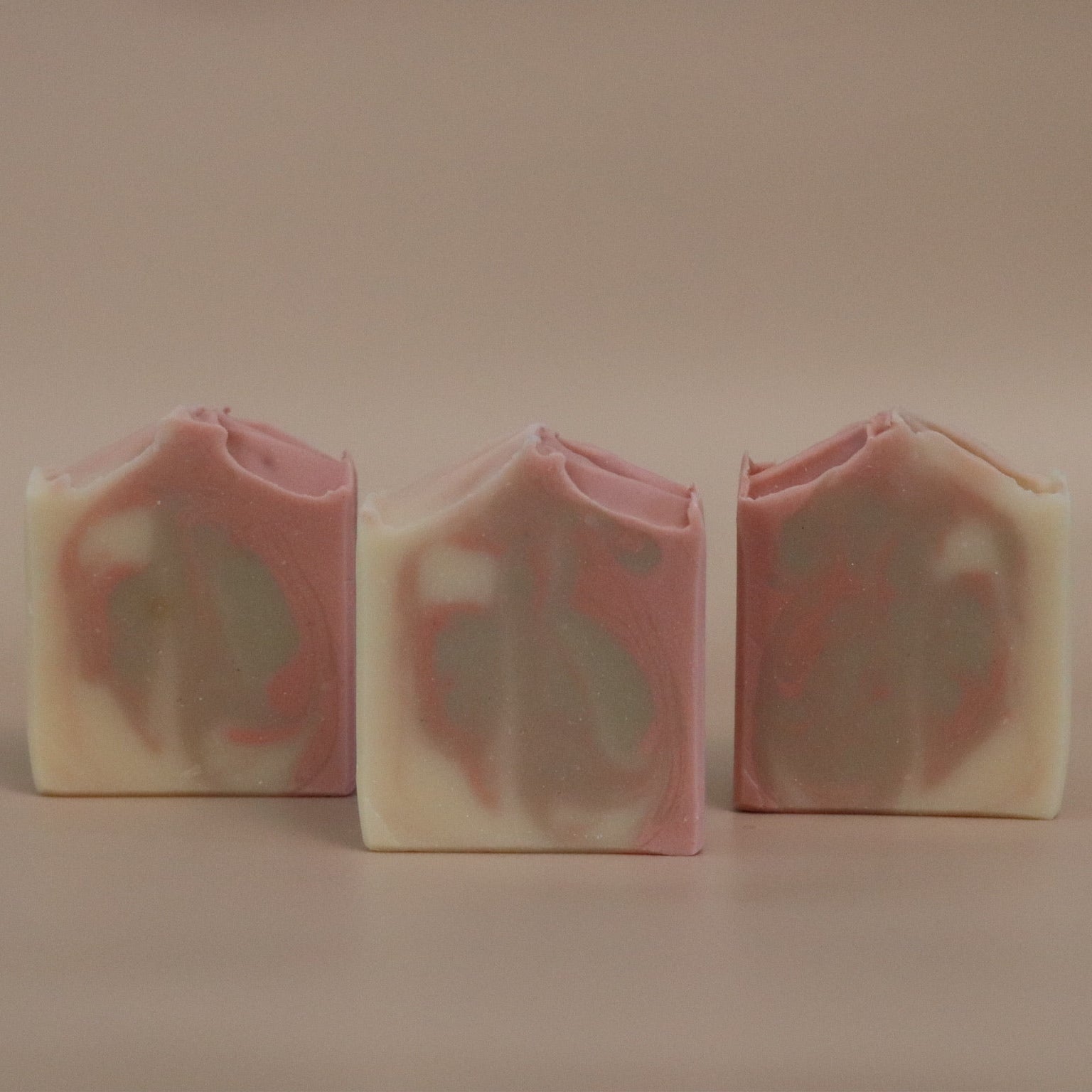 Three bars of soap with a pink, brown, and white marbled pattern on a beige background