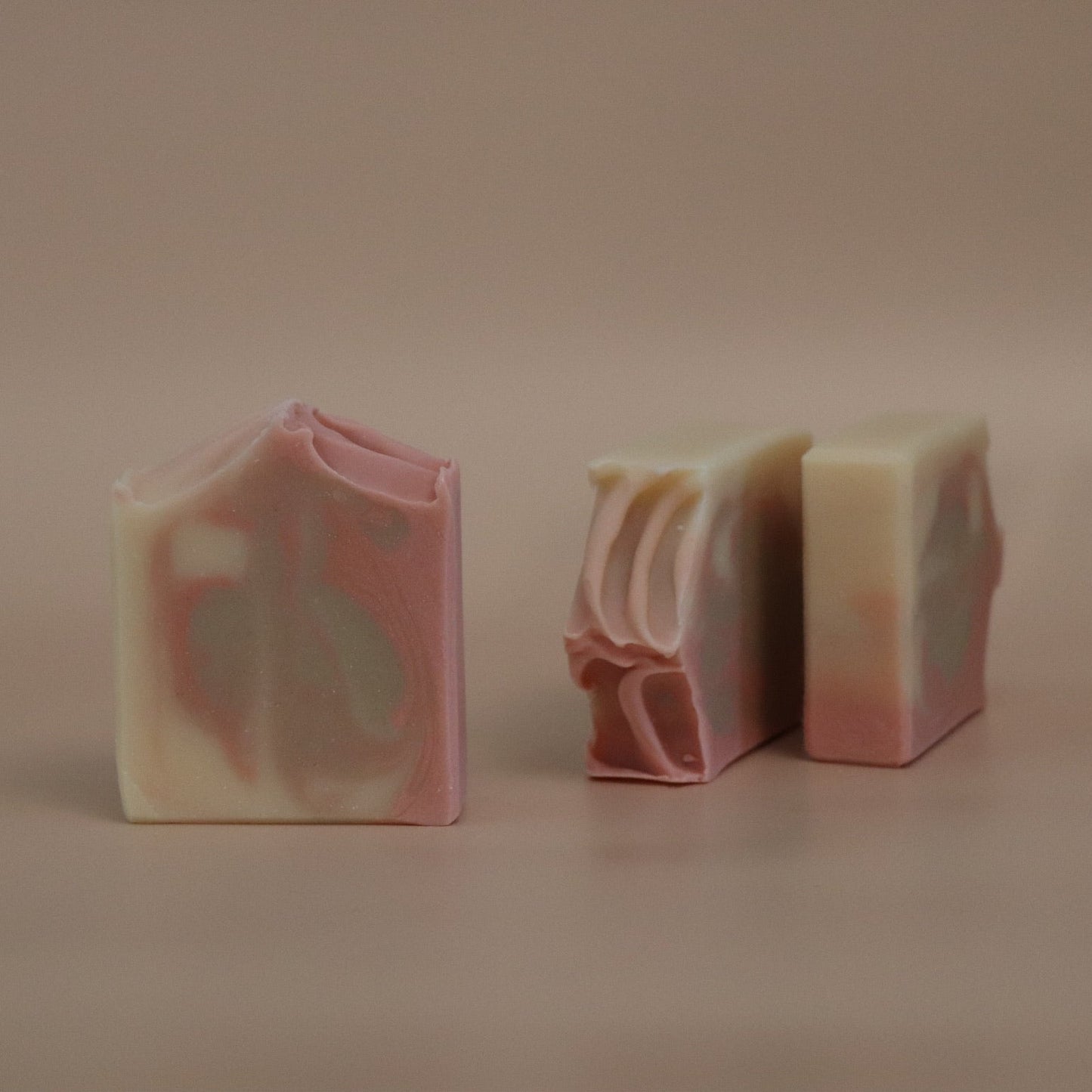 Three pink, sand brown, and white swirled soap bars on a beige background
