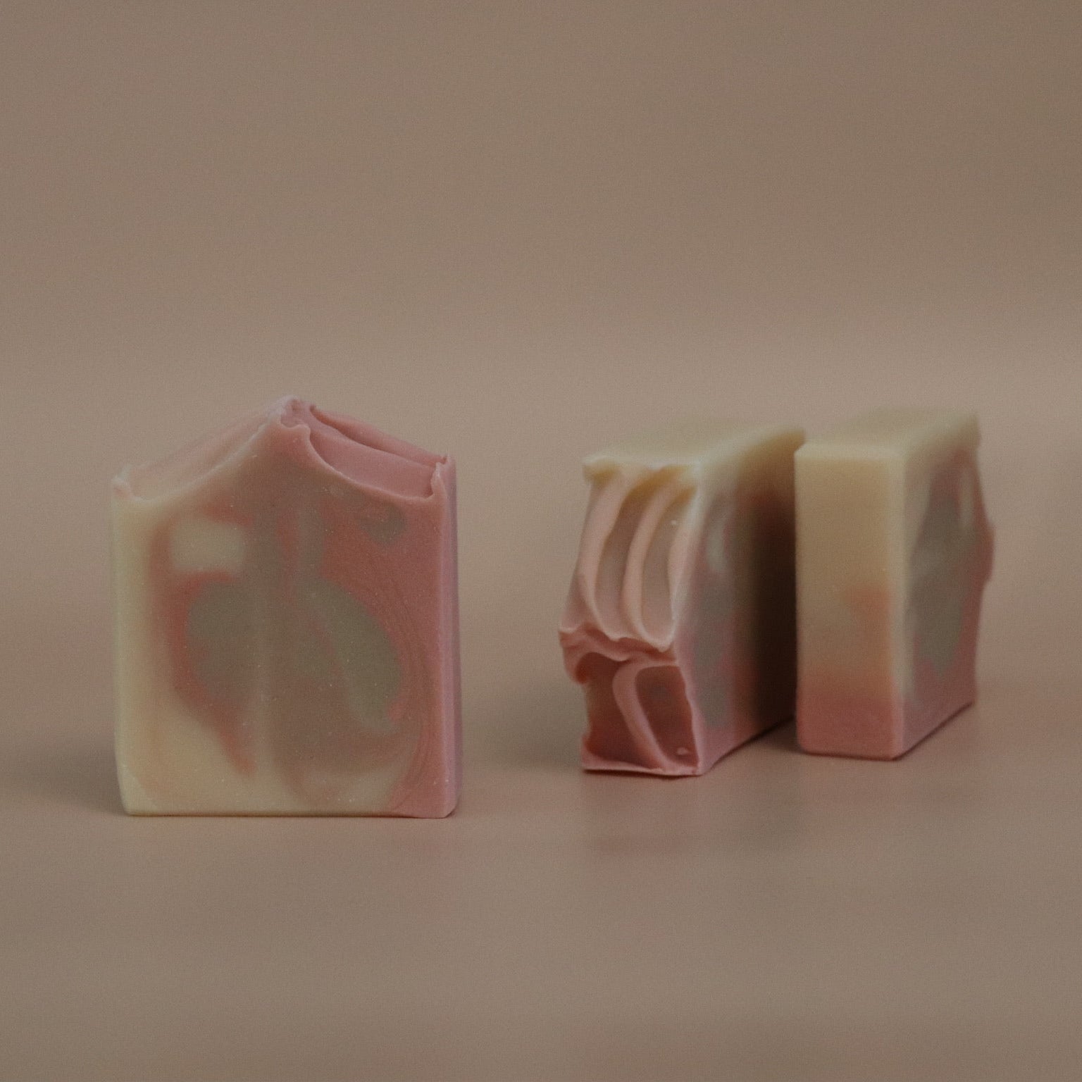 Three pink, sand brown, and white swirled soap bars on a beige background