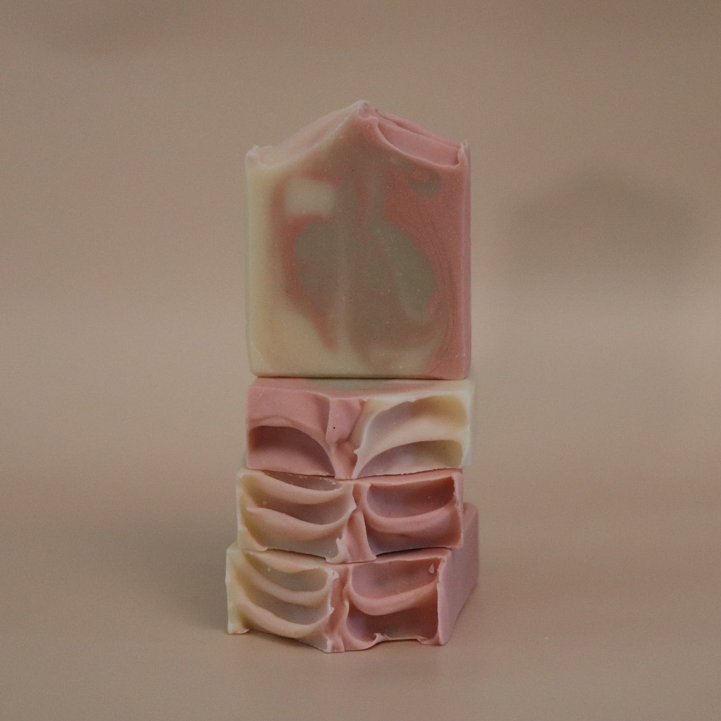 Stack of pink, beige, and cream  swirled layered soap bars on a brown background