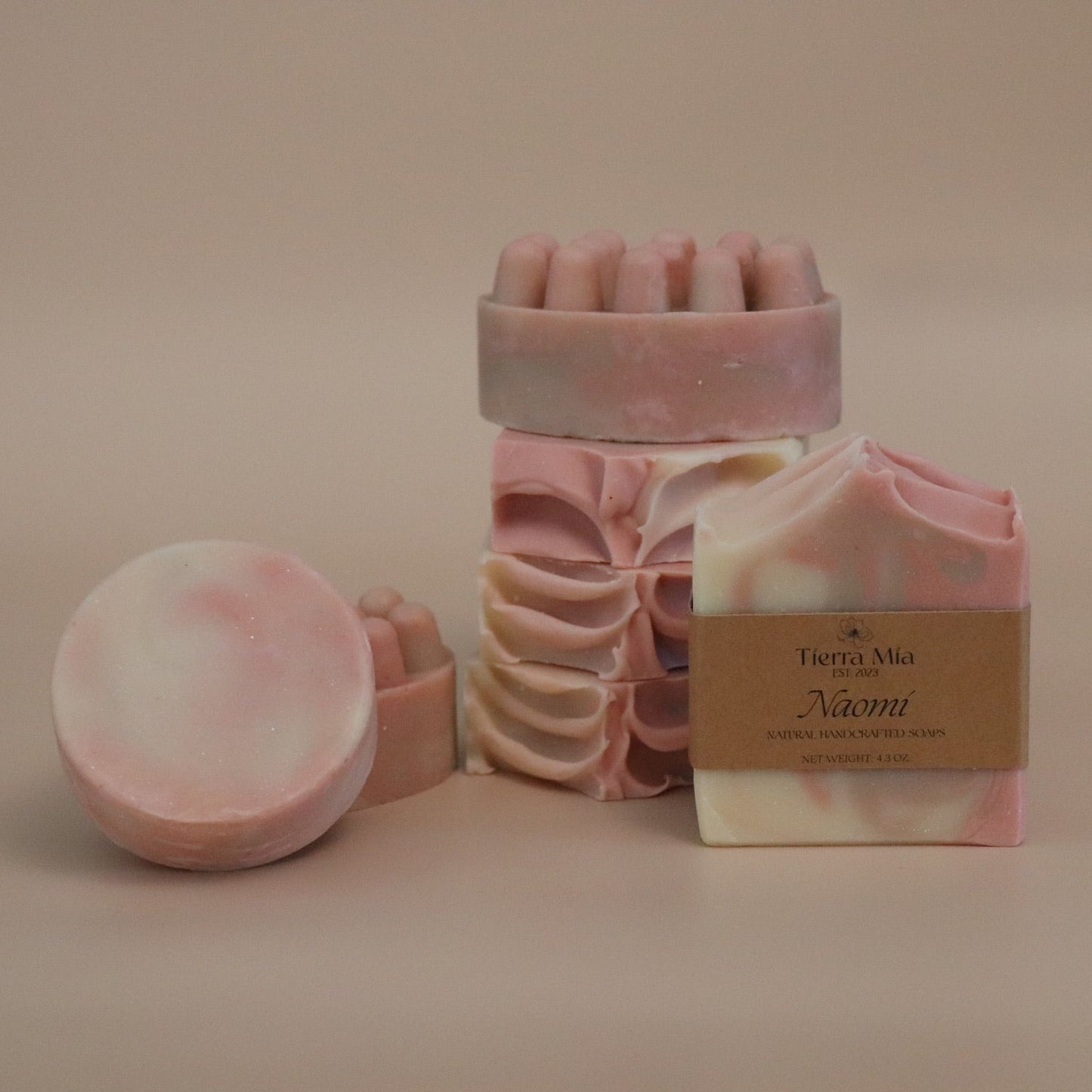 Pink soap products including a bar, a round bar and a massage bar on a beige background.