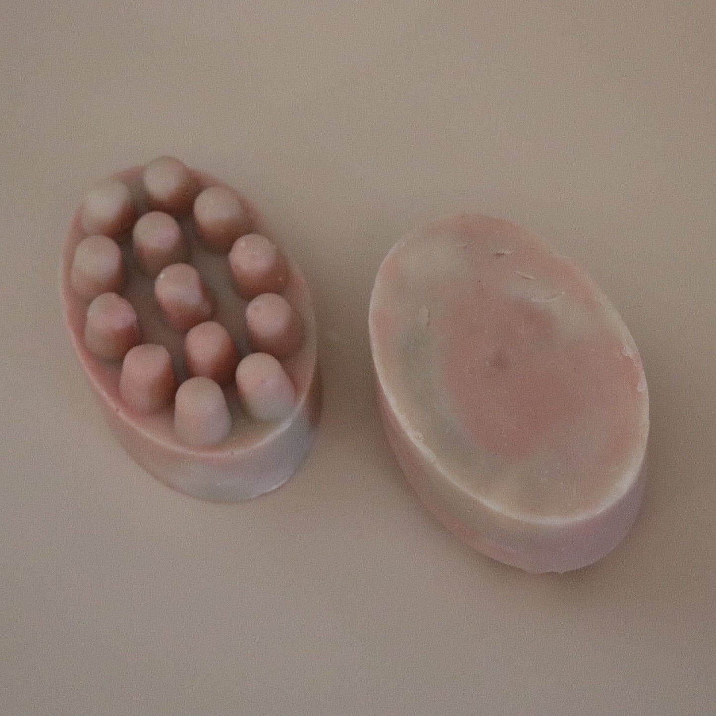 Two pink oval massage soap bars on a beige background